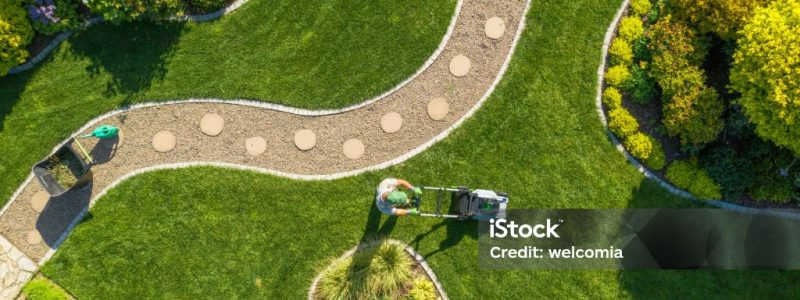 Aerial View of Big Garden Grass Field Mowing by Caucasian Gardener. Summer Time Landscape Maintenance.